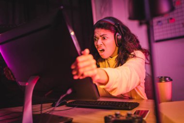 Kulaklıklı çılgın Afro-Amerikan oyuncu kahvenin yanında bilgisayar monitörü, bulanık ön planda akıllı telefon ve joystick. 