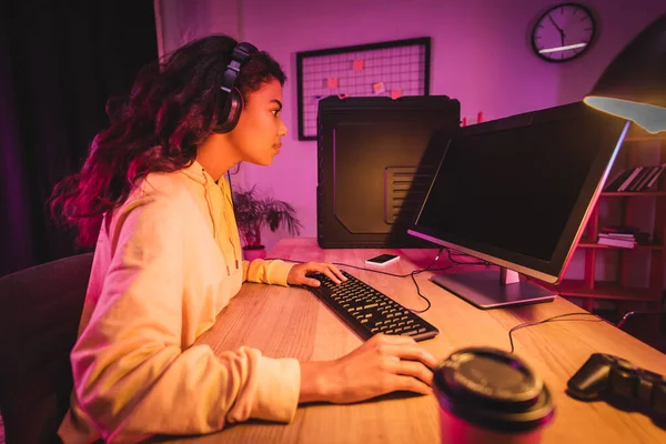 非洲裔美国游戏玩家在耳机上玩电脑游戏的侧视图 屏幕空白 靠近操纵杆 继续模糊的前景 — 图库照片