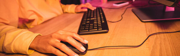 Cropped view of woman using computer mouse while playing video game on blurred background, banner