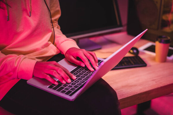 Обрезанный вид женщины с помощью ноутбука рядом с компьютером и кофе, чтобы перейти на размытый фон 