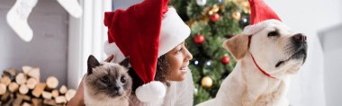 Gülümseyen Afrikalı Amerikalı kız. Noel Baba şapkalı. Labrador köpeğinin yanında.