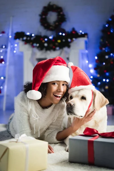 Excited African American Girl Santa Hat Stroking Labrador Dog While — Stock Photo, Image