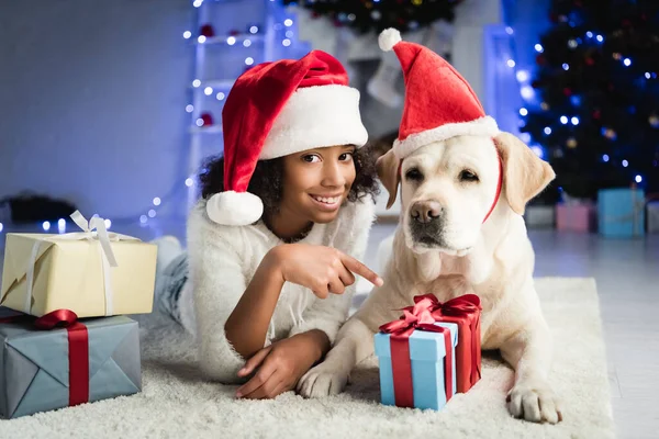 Cheerful African American Girl Pointing Finger Gift Box While Lying — Stock Photo, Image