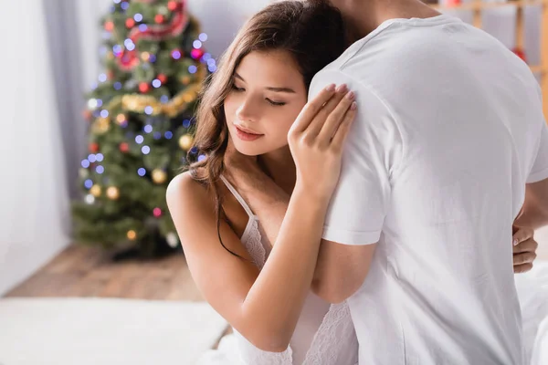 Junge Frau Umarmt Freund Mit Geschmücktem Weihnachtsbaum Auf Verschwommenem Hintergrund — Stockfoto