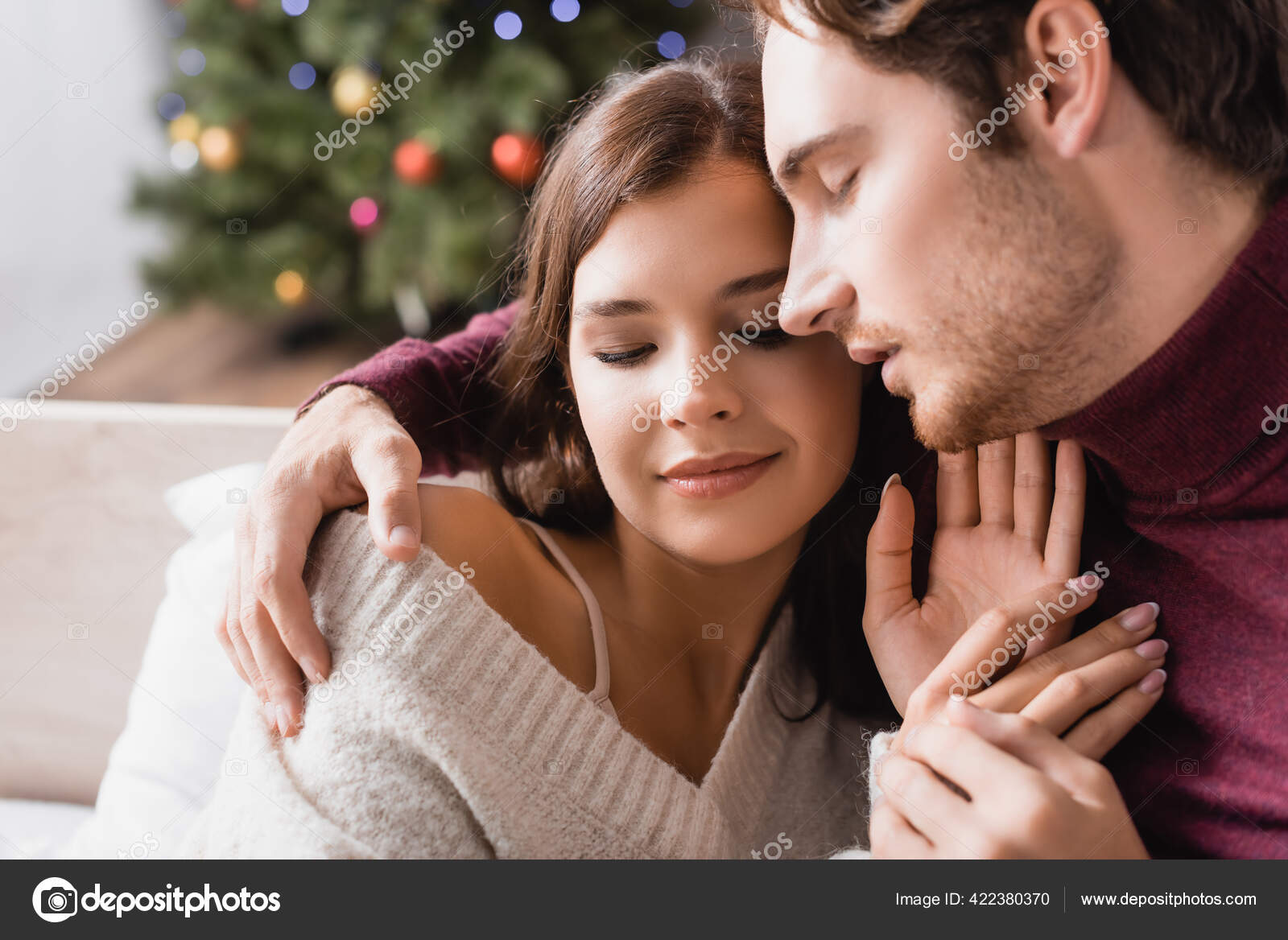 Pleased Couple Cozy Sweaters Hugging Decorated Christmas Tree Blurred