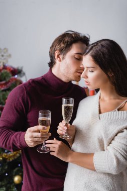 Tutkulu bir çift ellerinde şampanya bardakları ve bulanık arka planda noel ağacı.