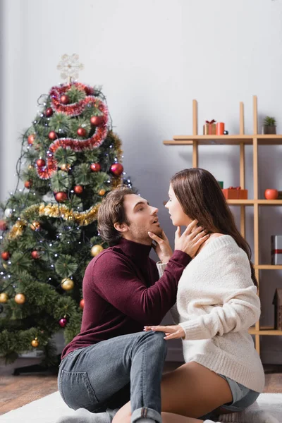 在模糊的背景下 一对充满热情的夫妇拥抱在圣诞树旁的侧视图 — 图库照片