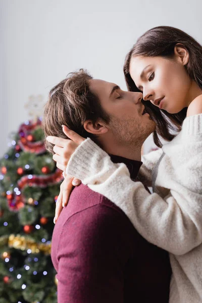 Passionate Man Embracing Girlfriend Sweater Christmas Tree Blurred Background — Stock Photo, Image