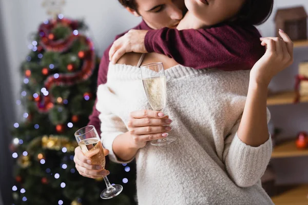 クリスマスツリーの近くでシャンパンで眼鏡をかけながら情熱的な男のキス女性のクロップドビュー — ストック写真