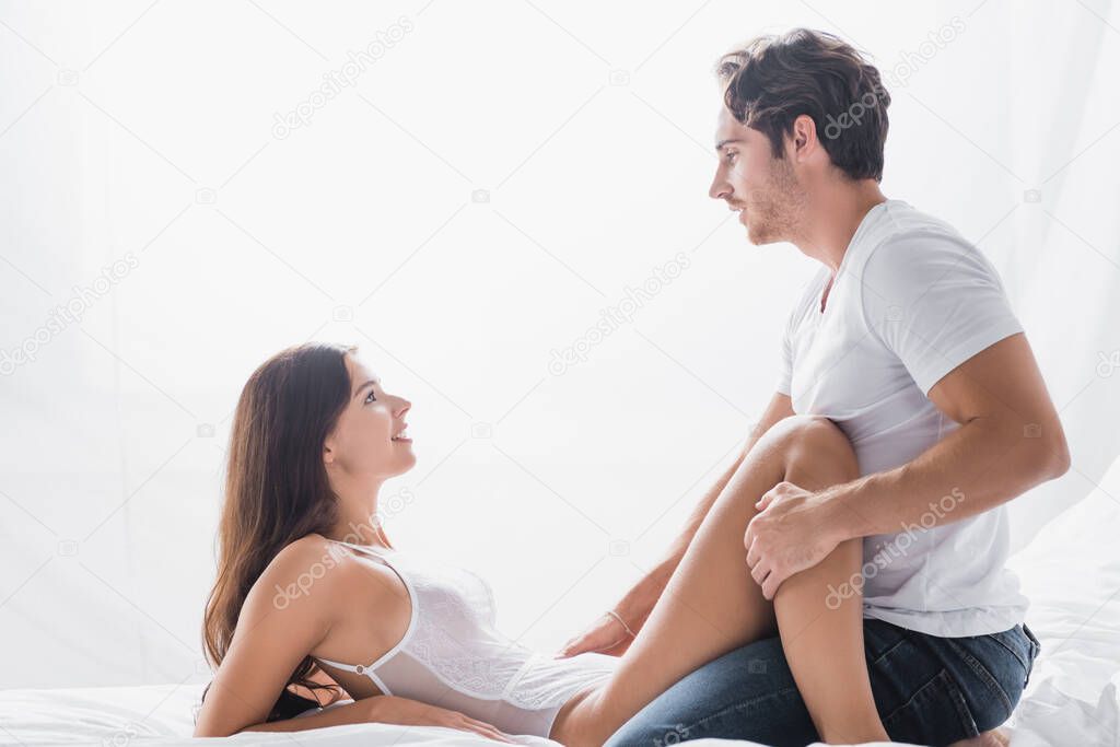 side view of passionate man looking at pleased girlfriend in bodysuit 