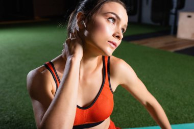 Spor merkezine bakarken kulaklığı boynunu ısıtan sporcu kadın.