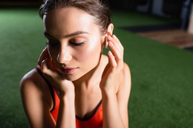 Genç sporcu kadın spor salonunda müzik dinlerken kablosuz kulaklığa dokunuyor.