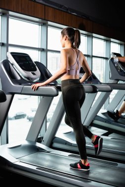 athletic sportswoman in leggings running on treadmill in sports center clipart