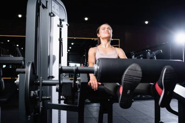 tense sportswoman working out on leg extension machine in gym clipart