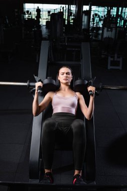Atletik sporcu kadının eğitim makinesinde silah geliştirme egzersizi yaparken yüksek açılı görüntüsü