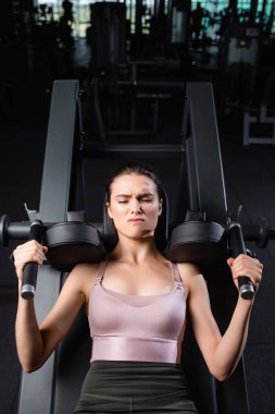 top view of sportswoman with closed eyes training on arms extension machine in gym clipart