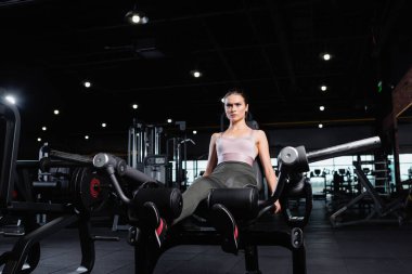 Sportif, genç bir kadın spor salonunda bacak uzatma makinesinde egzersiz yapıyor.