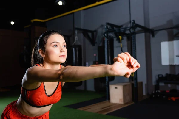 Ung Sportskvinde Strækker Armene Mens Man Ser Væk Fitnesscentret - Stock-foto