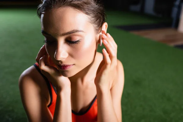 Young Sportswoman Touching Wireless Earphone While Listening Music Gym — Stock Photo, Image