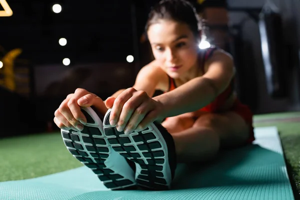 年轻的女运动员一边摸运动鞋 一边在模糊的背景下伸展着身体垫 — 图库照片
