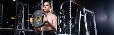 athletic sportswoman working out with weight disk in sports center, banner clipart