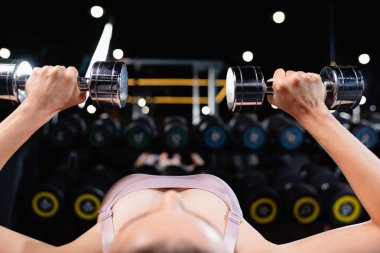 Spor kadını dambıllarla egzersiz yapıyor bulanık ön planda yatıyor.