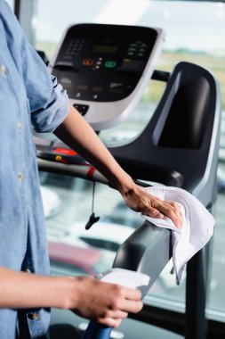 Koşu bandını spor salonunda bez parçasıyla silen gündelikçi kadının kısmi görüntüsü