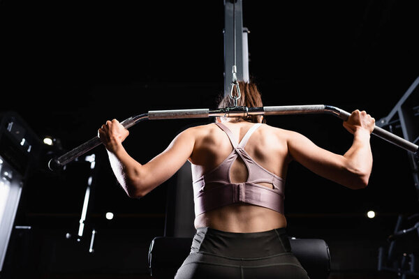 back view of sportive woman doing arms and back extension exercise on lat machine