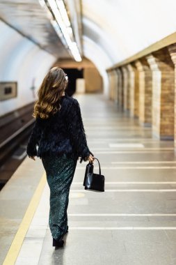 Metro platformu boyunca uzun lurex elbiseli şık bir kadının arka plan görüntüsü