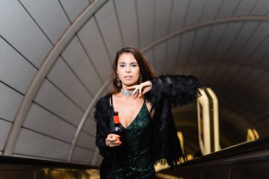 cropped view of glamour woman posing on escalator with bottle of wine clipart