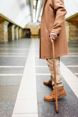 cropped view of man with walking stick, in autumn outfit, standing at metro station clipart