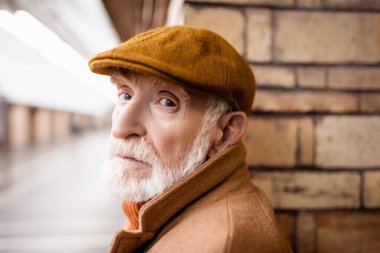 Güz şapkalı yaşlı adam metro istasyonundaki kameraya bakıyor.