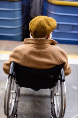Tekerlekli sandalyedeki yaşlı engelli adamın arka görüntüsü bulanık tren istasyonunda paltosu ve şapkası vardı.