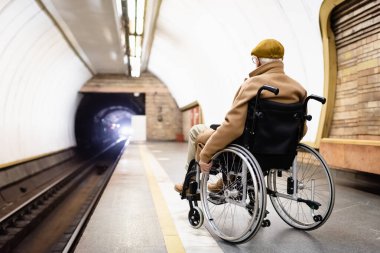 Sonbahar giysileri içinde metro platformunda tüneldeki ışığa bakan yaşlı adamın arka görüntüsü