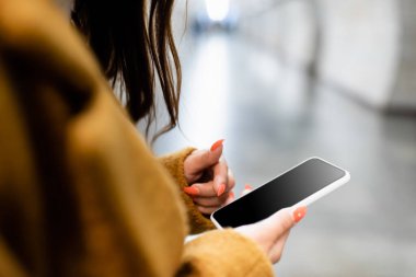 Ön planda boş ekranlı akıllı telefonu tutan kadının kısmi görüntüsü