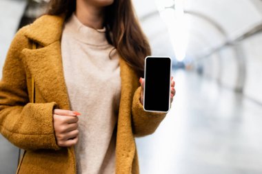Güz kıyafetleri içindeki kadının metro istasyonunda boş ekranlı akıllı telefonu gösteren kısmi görüntüsü