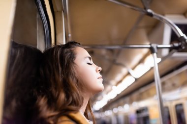 young woman travelling in metro train with closed eyes on blurred foreground clipart