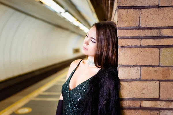 sensual young woman leaning on brick column while standing on metro platform