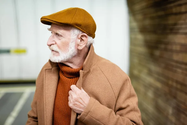 Senior Man Cap Touching Collar Autumn Coat While Standing Metro — Foto de Stock