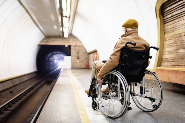 back view of elderly man in autumn clothes on metro platform looking at light in tunnel