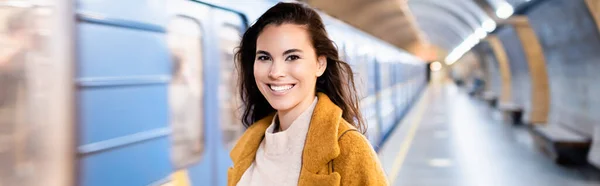 stock image happy young woman looking at camera on underground platform with blurred train, banner