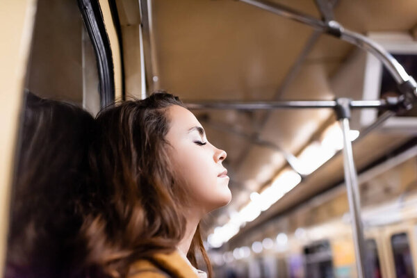 young woman travelling in metro train with closed eyes on blurred foreground