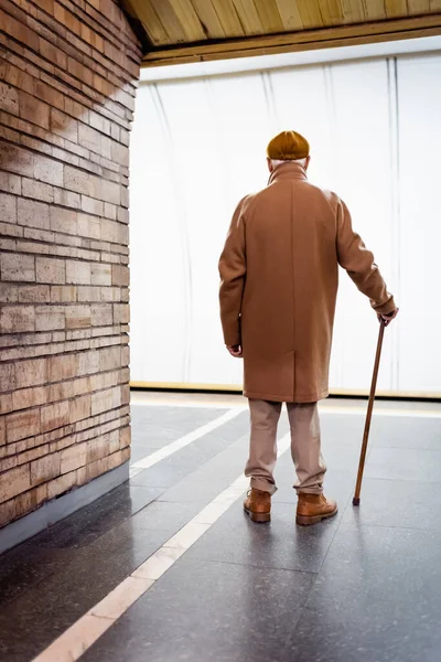 Back view of aged man with walking stick, wearing autumn clothes, standing on subway platform — Stock Image Back View Aged Man Walking Stick Wearing Autumn Clothes Standing Stock Photo