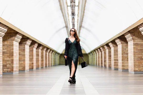 Seductive woman in long black dress walking along metro station with wine bottle and handbag — Stock Image Seductive Woman Long Black Dress Walking Metro Station Wine Bottle Royalty Free Stock Photos
