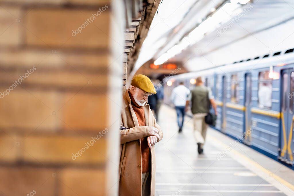 senior man in autumn coat and cap standing on underground platform on blurred foreground