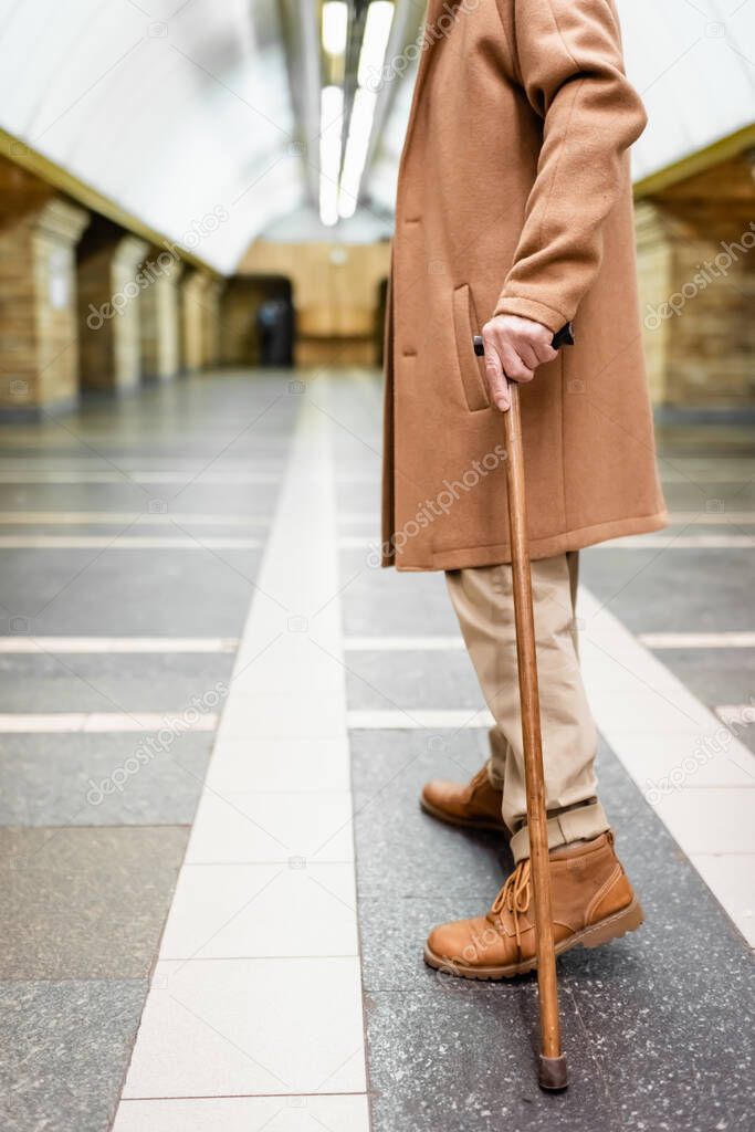 cropped view of man with walking stick, in autumn outfit, standing at metro station