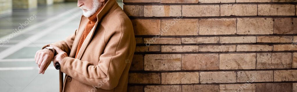 Cropped view of elderly man in coat looking at wristwatch while standing near column at underground station, banner — Stock Image Cropped View Elderly Man Coat Looking Wristwatch While Standing Column Royalty Free Stock Images
