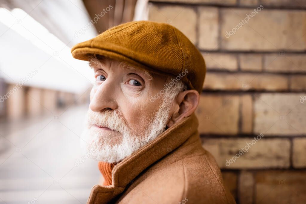 aged man in autumn cap looking at camera on metro platform
