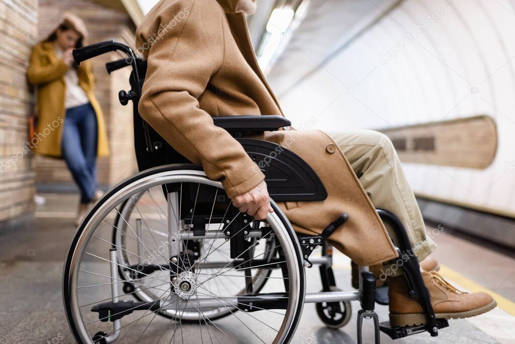 side view of elderly disabled man on metro platform, and woman on blurred background