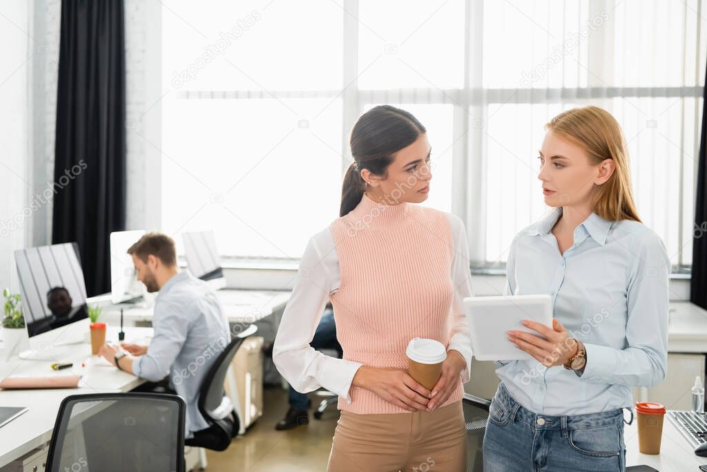 Businesswoman with digital tablet and coffee to go looking at each other in office 
